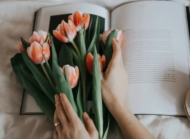 A person holding flowers in front of an open book.