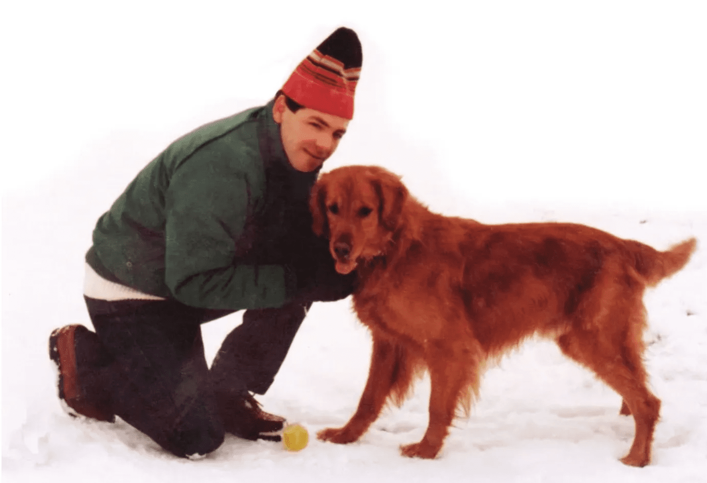 A man kneeling down next to a dog.